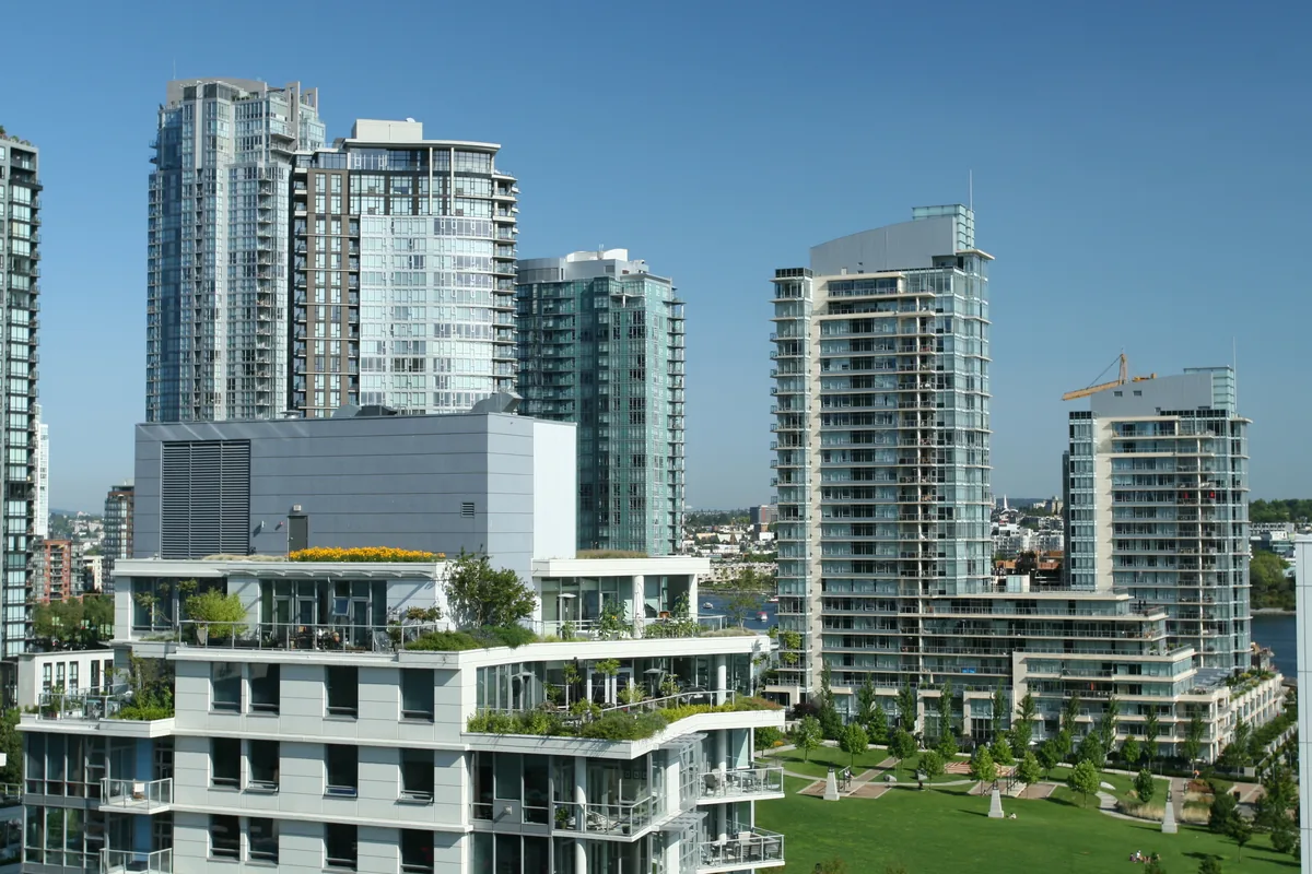 Modern glass residential towers with landscaped terraces under a clear blue sky