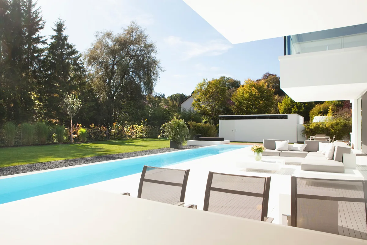 Serene infinity-edge pool beside a white modern villa with a landscaped garden under a clear sky