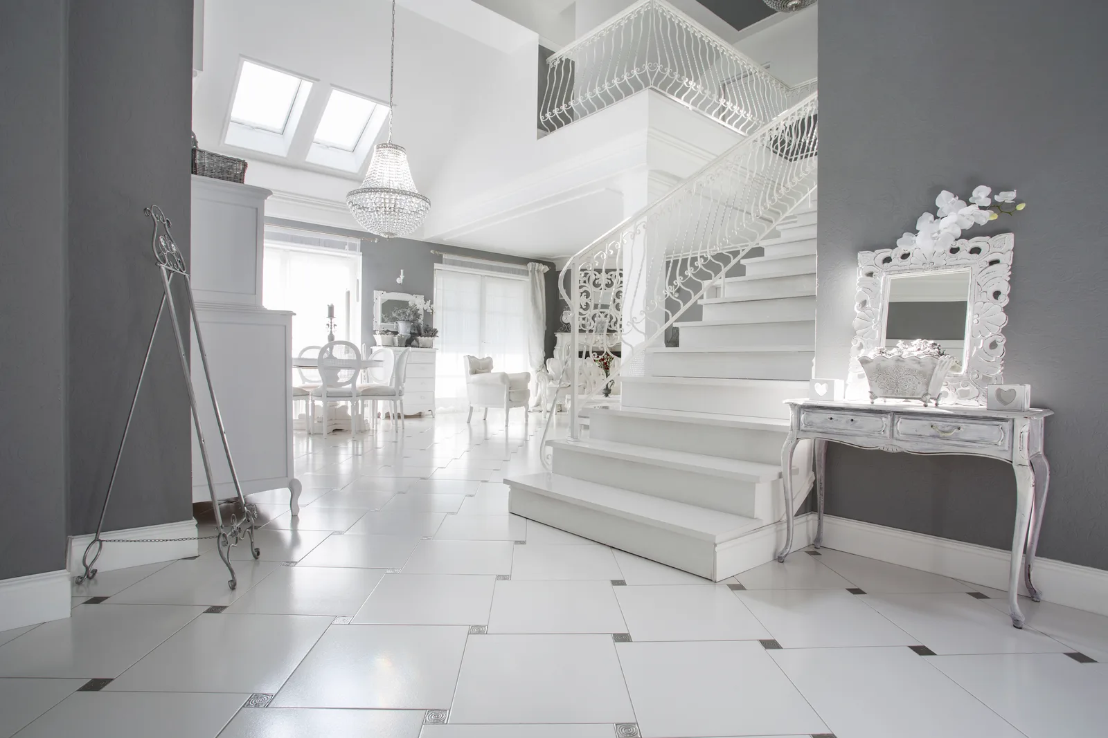 Bright, grand white designer interior with a sweeping staircase, crystal chandelier and marble floor
