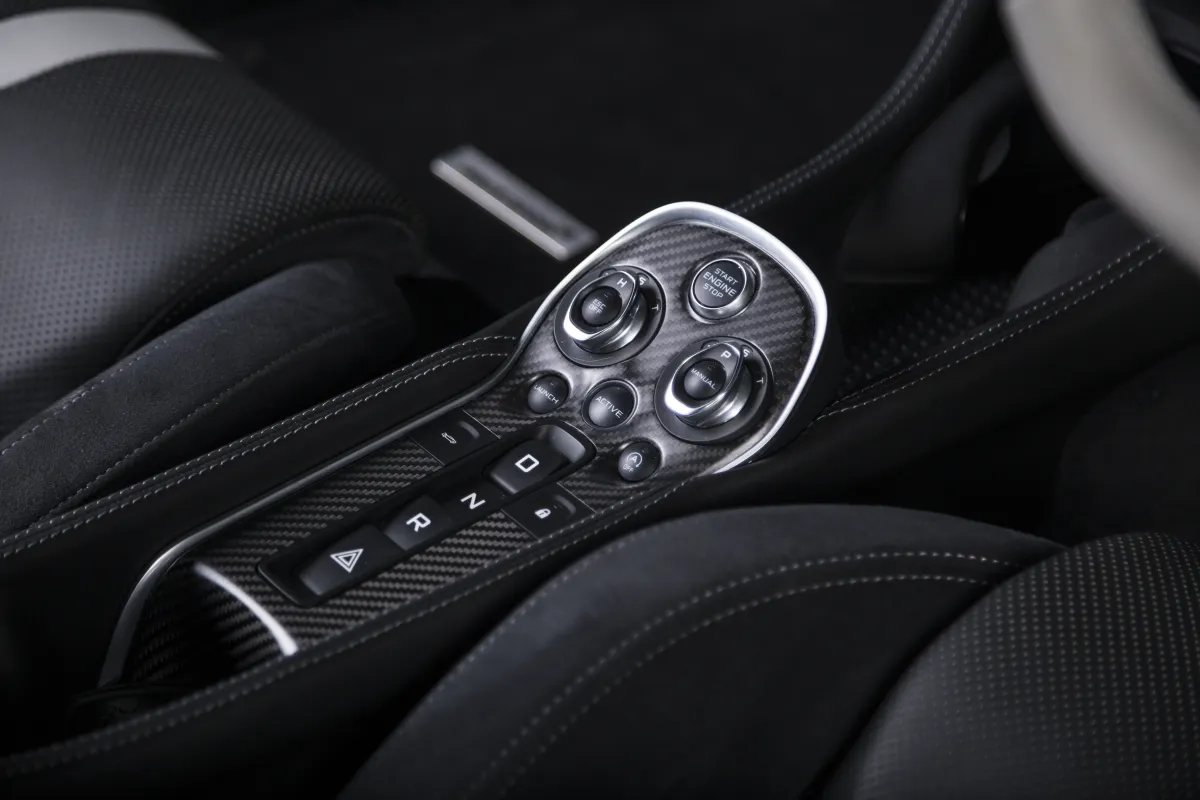 Close-up of a luxury sports car cockpit with carbon-fibre trim, brushed switchgear and quilted leather stitching