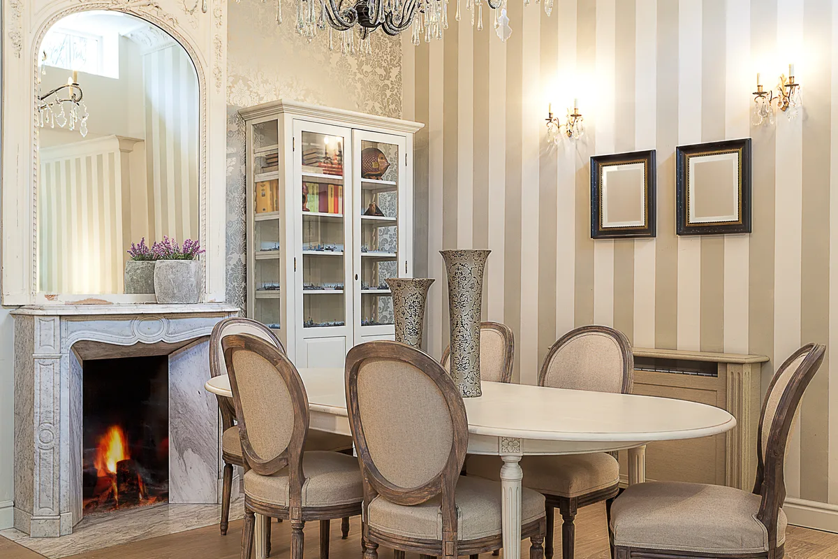 Formal residence dining room with a marble fireplace, crystal chandelier and an oval table set with upholstered chairs