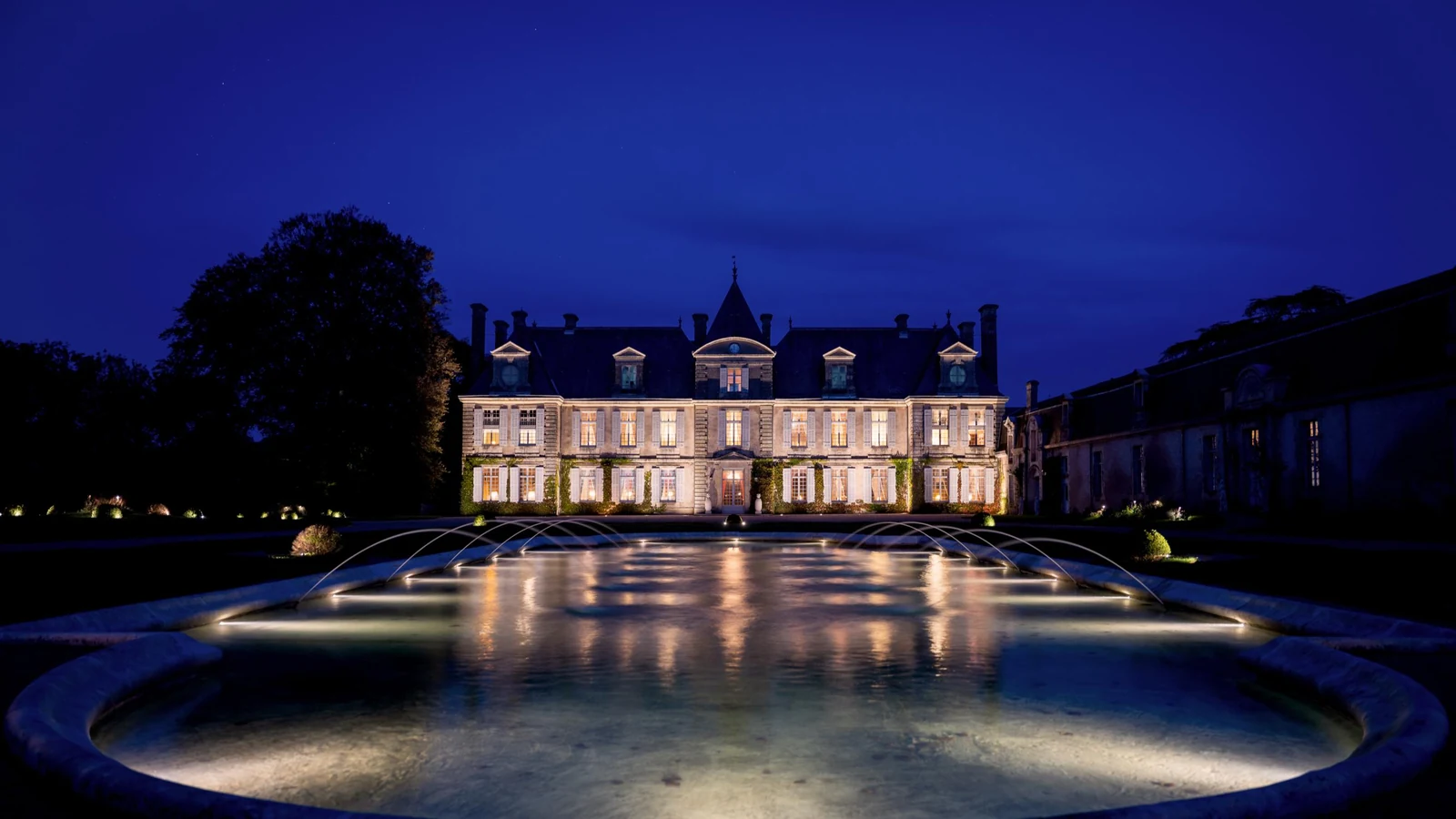 Private château estate façade illuminated at night reflected in the fountain basin
