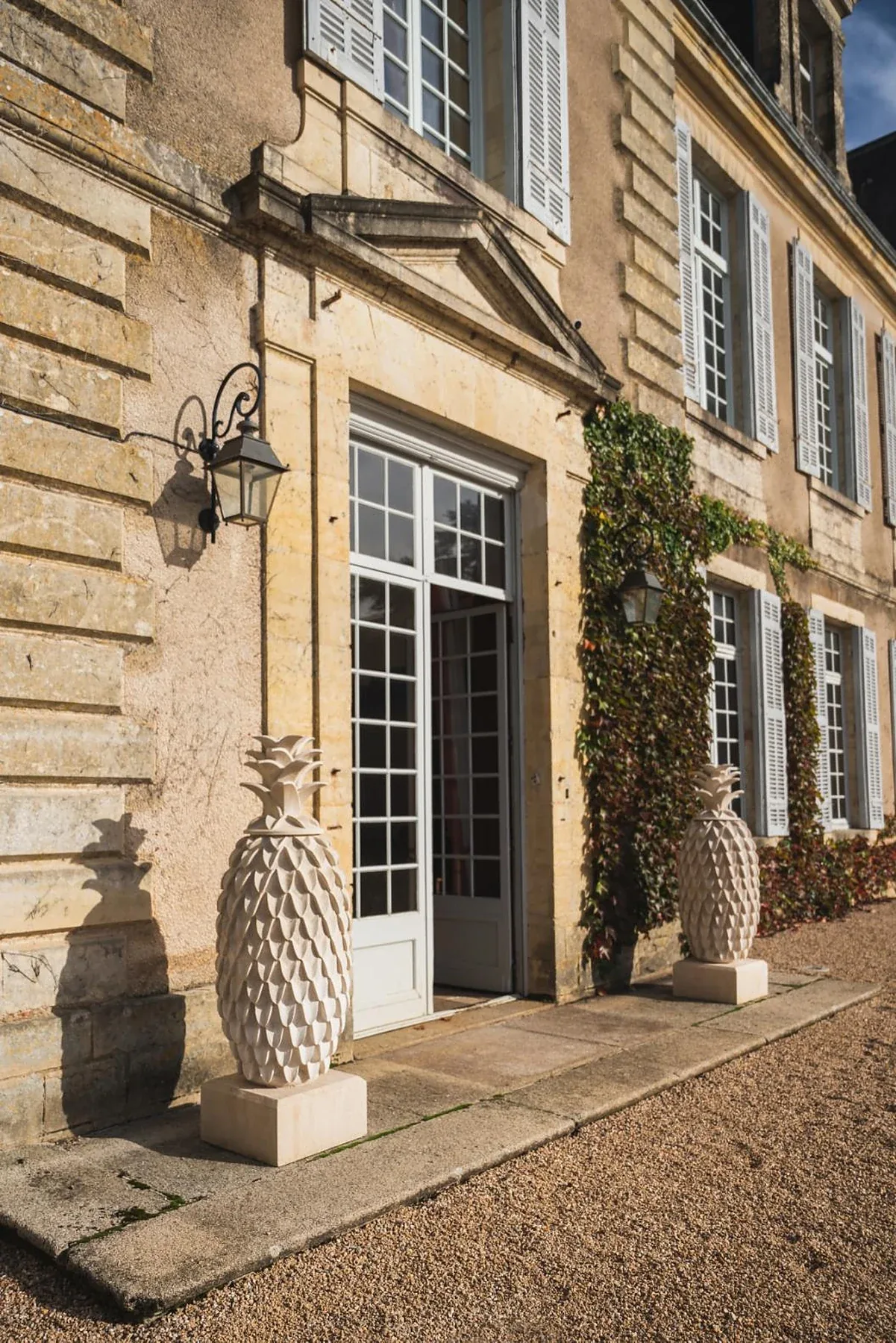 Private château estate entrance doorway with carved stone pineapple finials and iron lantern