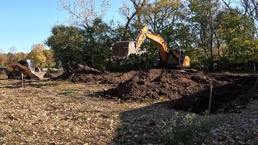 Excavator digging on a cleared site surrounded by trees