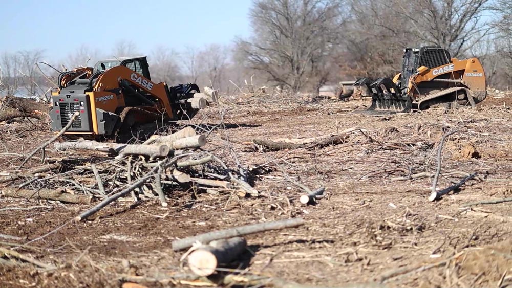 Two forestry mulchers working among cut logs and brush piles on a cleared lot