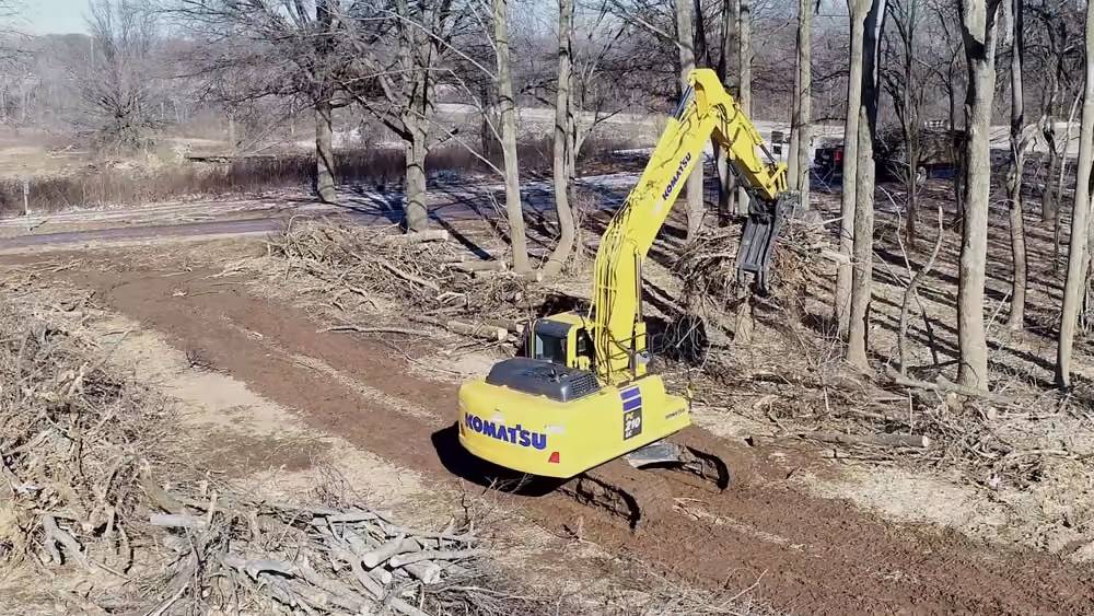 Yellow excavator on a dirt path cut through the woods