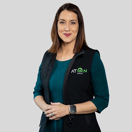 Smiling woman with shoulder-length brown hair wearing a teal dress and black ATON Solar vest.