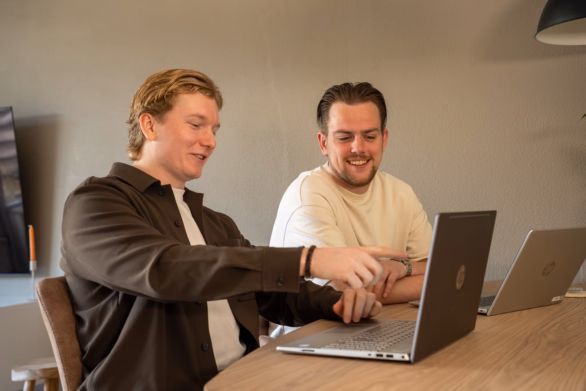 Timo en Stan van SENT Marketing zitten lachend aan tafel en bekijken proactief de resultaten op een laptop, waarbij één van hen naar het scherm wijst.