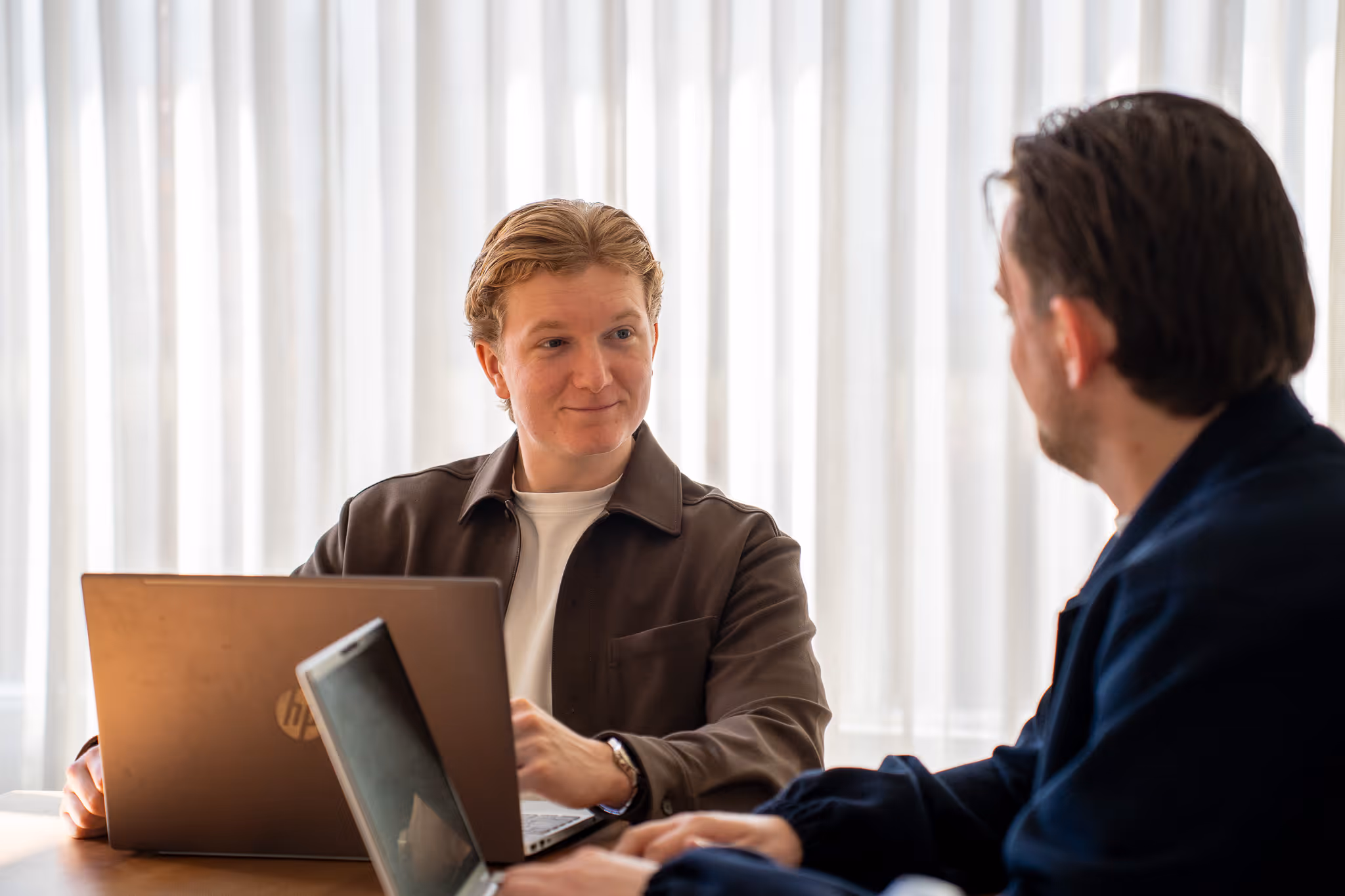 Timo en Stan van SENT Marketing in gesprek aan een werktafel, waarbij ze de marketingstrategie op hun laptops afstemmen om de klant volledig te ontzorgen.