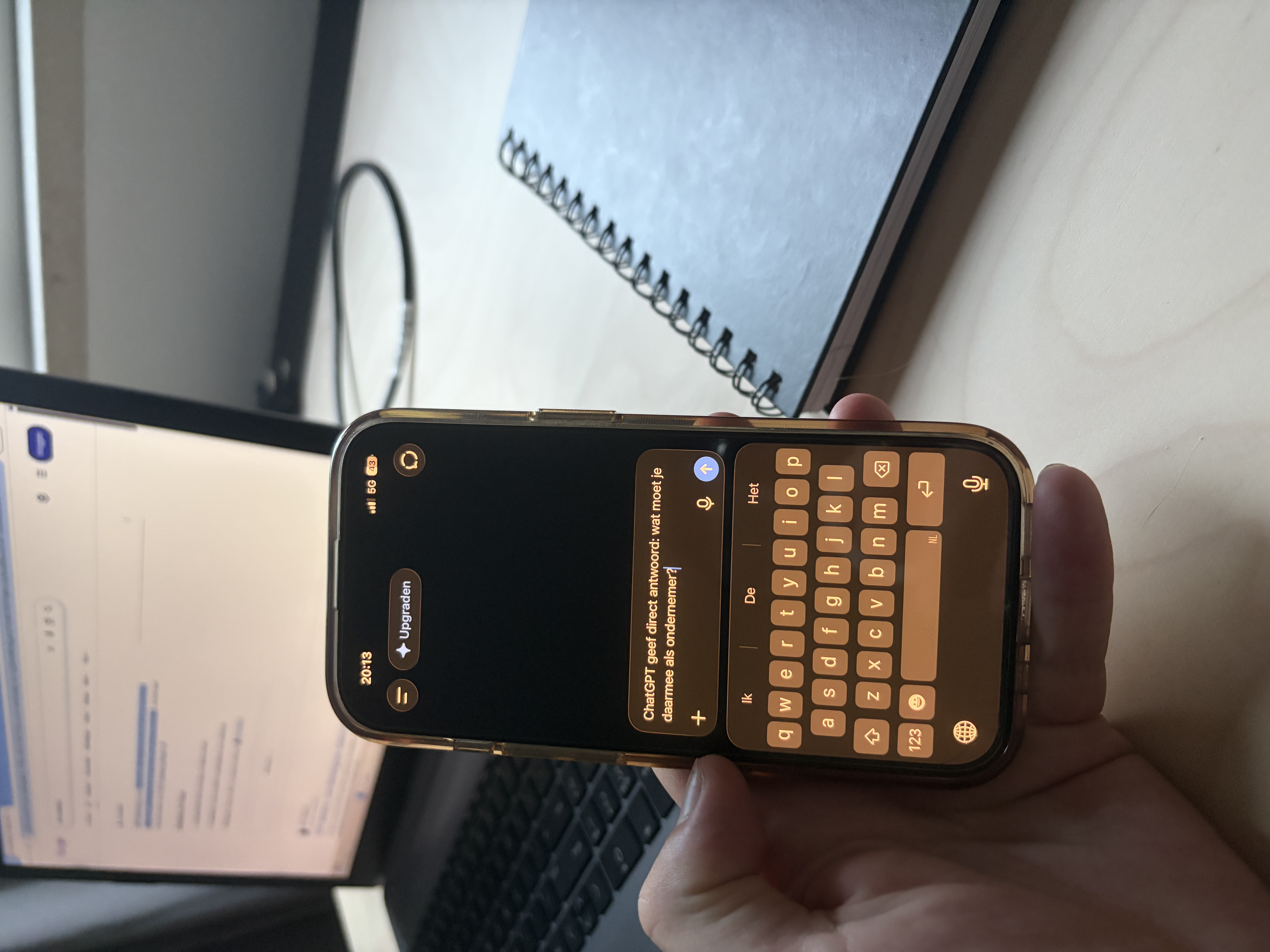 Hand houdt telefoon met ChatGPT-app vast voor een laptop op een bureau