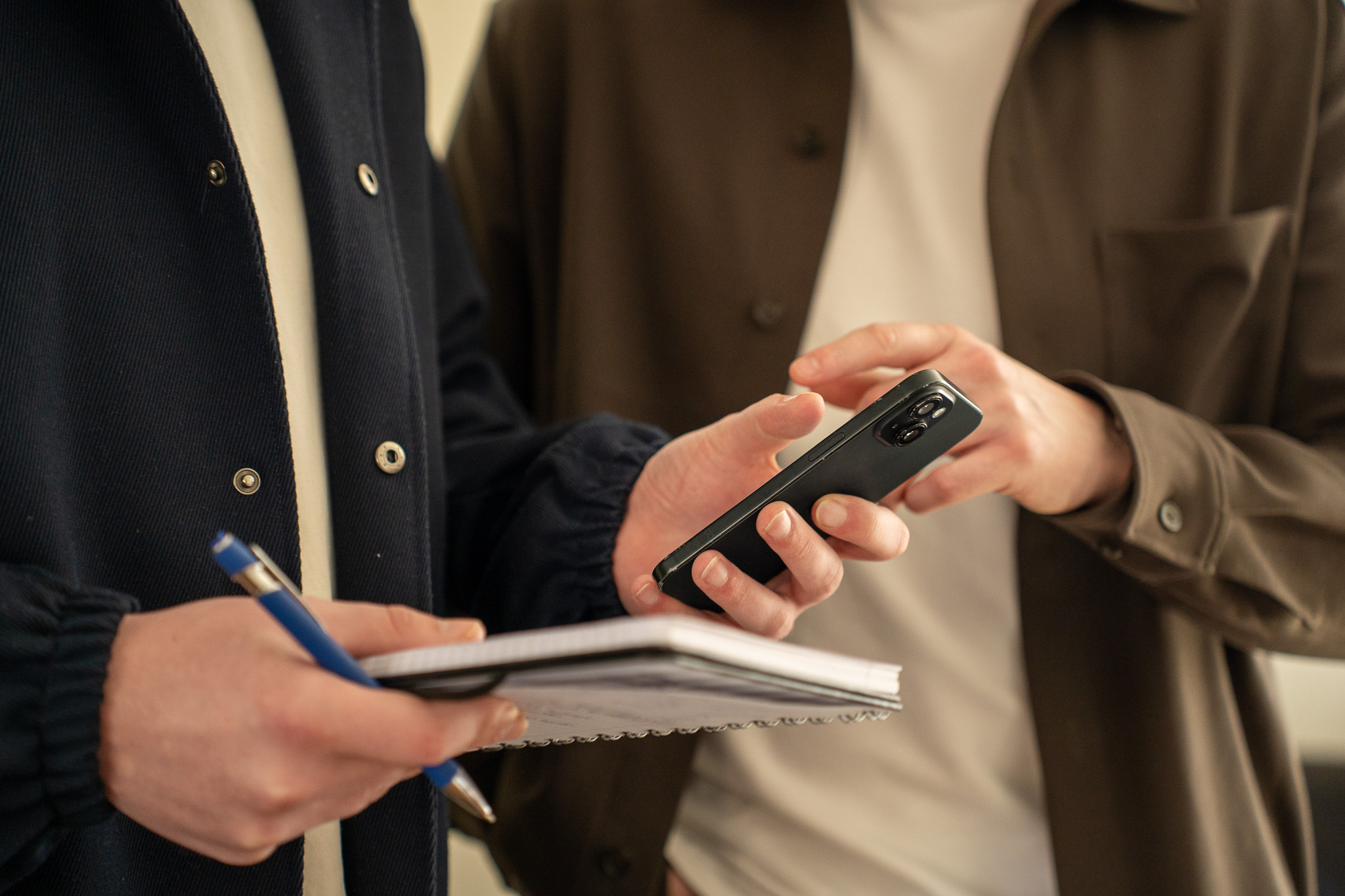 Timo en Stan van SENT Marketing stemmen een social media campagne af; de één bedient een smartphone terwijl de ander aantekeningen maakt op een notitieblok.