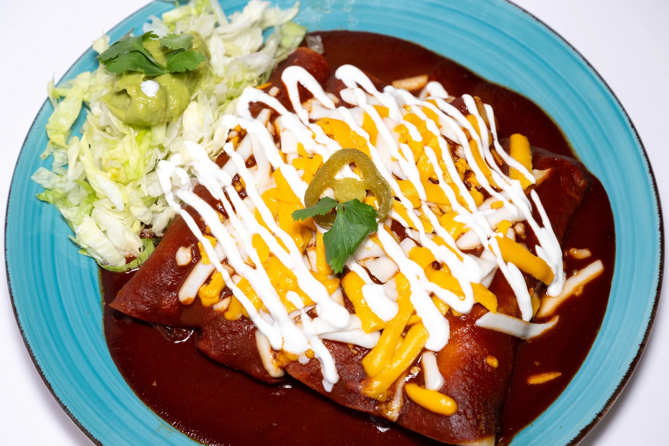 red enchiladas with sour cream and cheese on top, and salad on the side