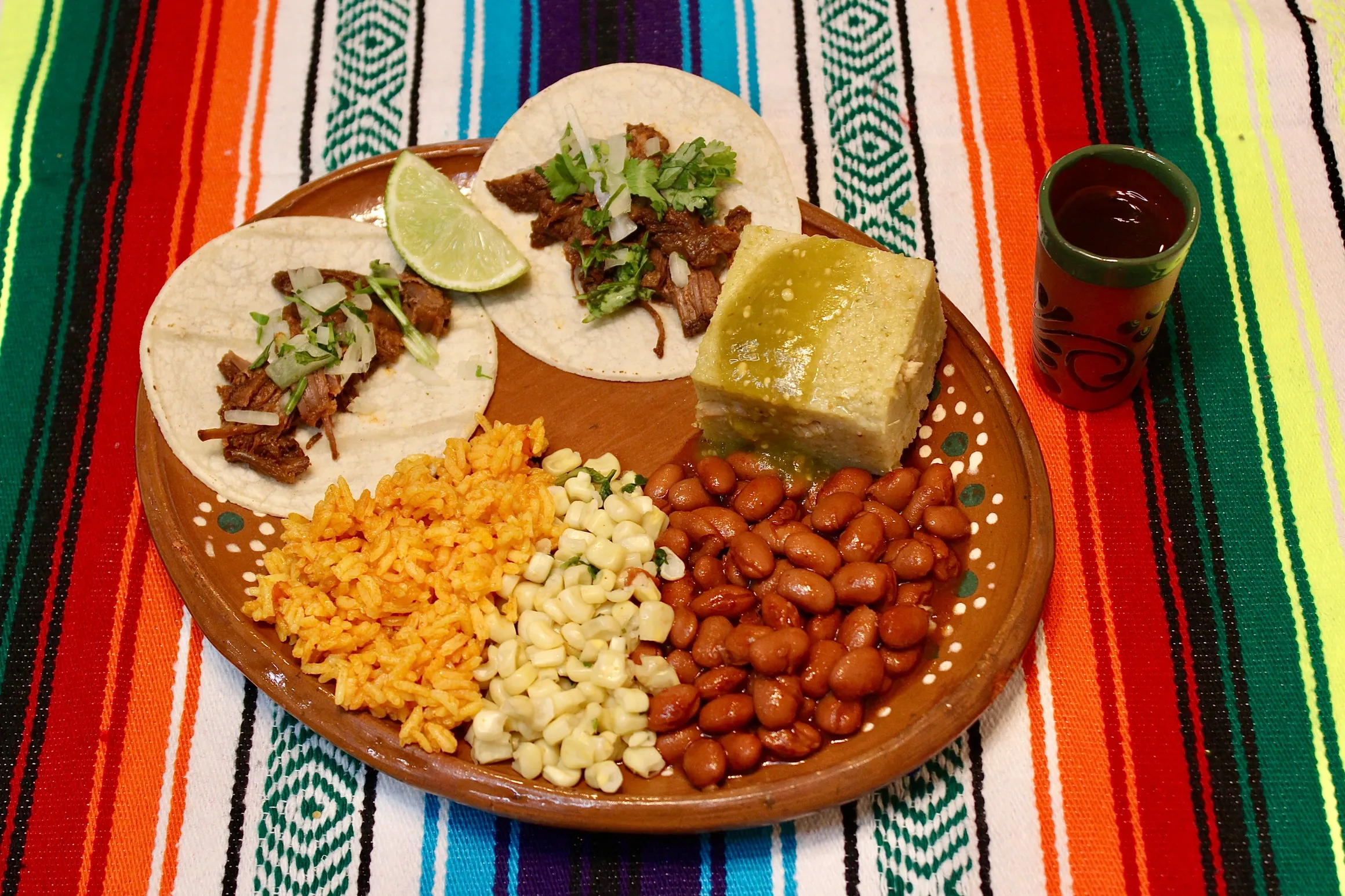 plate with 2 tacos, rice, beans, corn and a piece of tamale