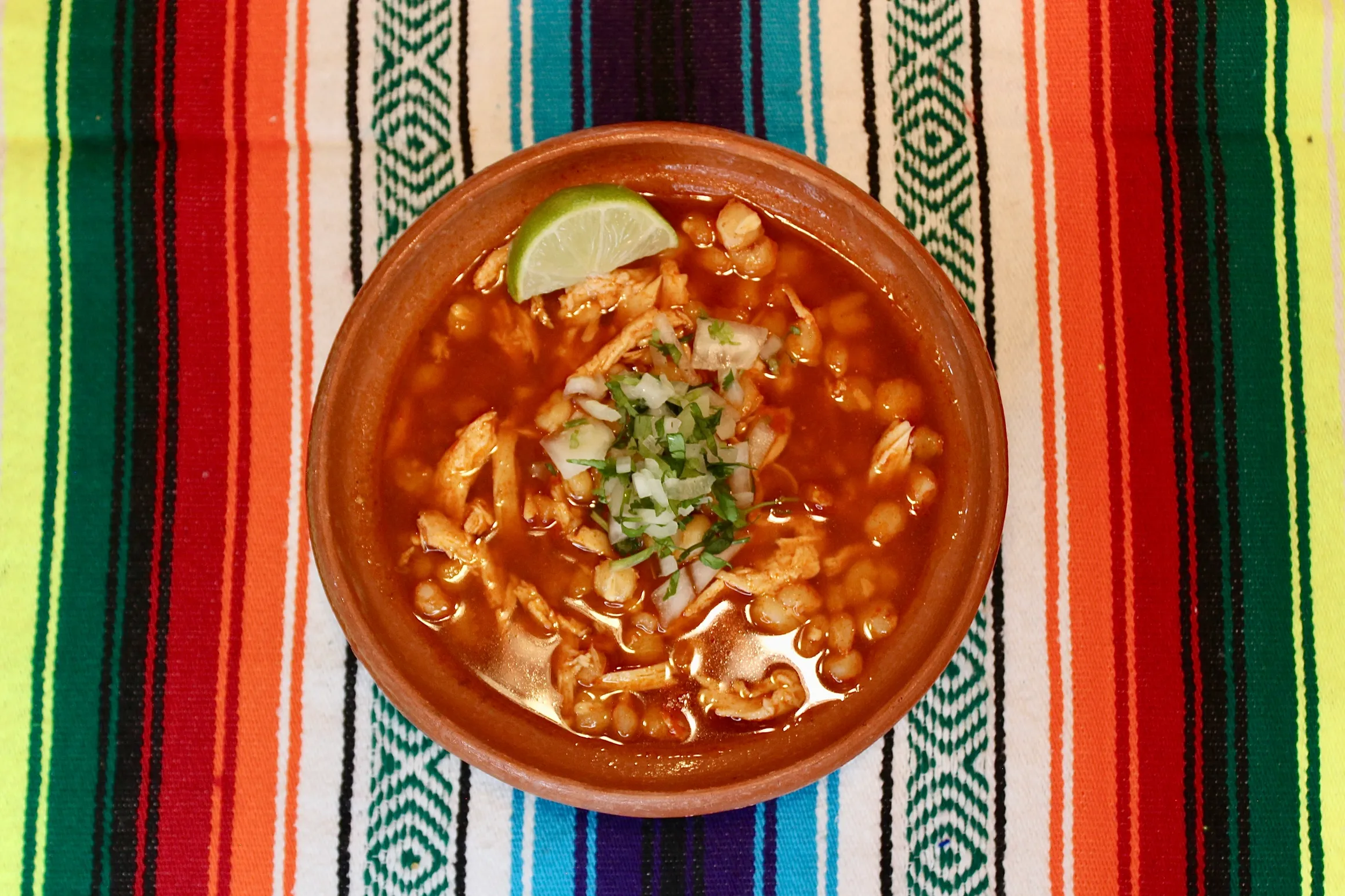 plate of red pozole with lettuce and a slice of lemon