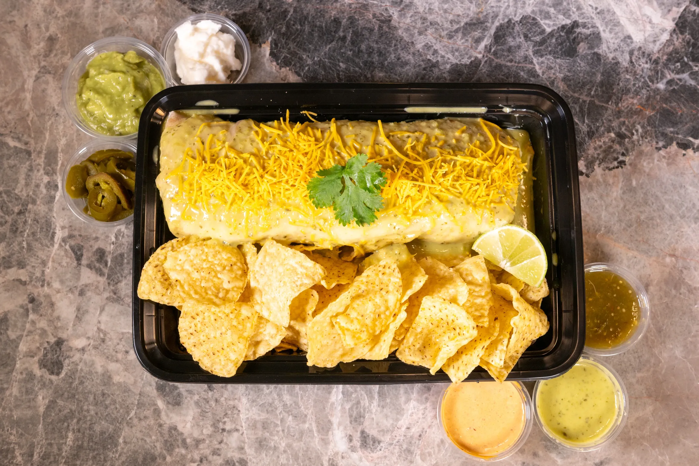 burrito in green sauce with cheese on top and tortilla chips on the side