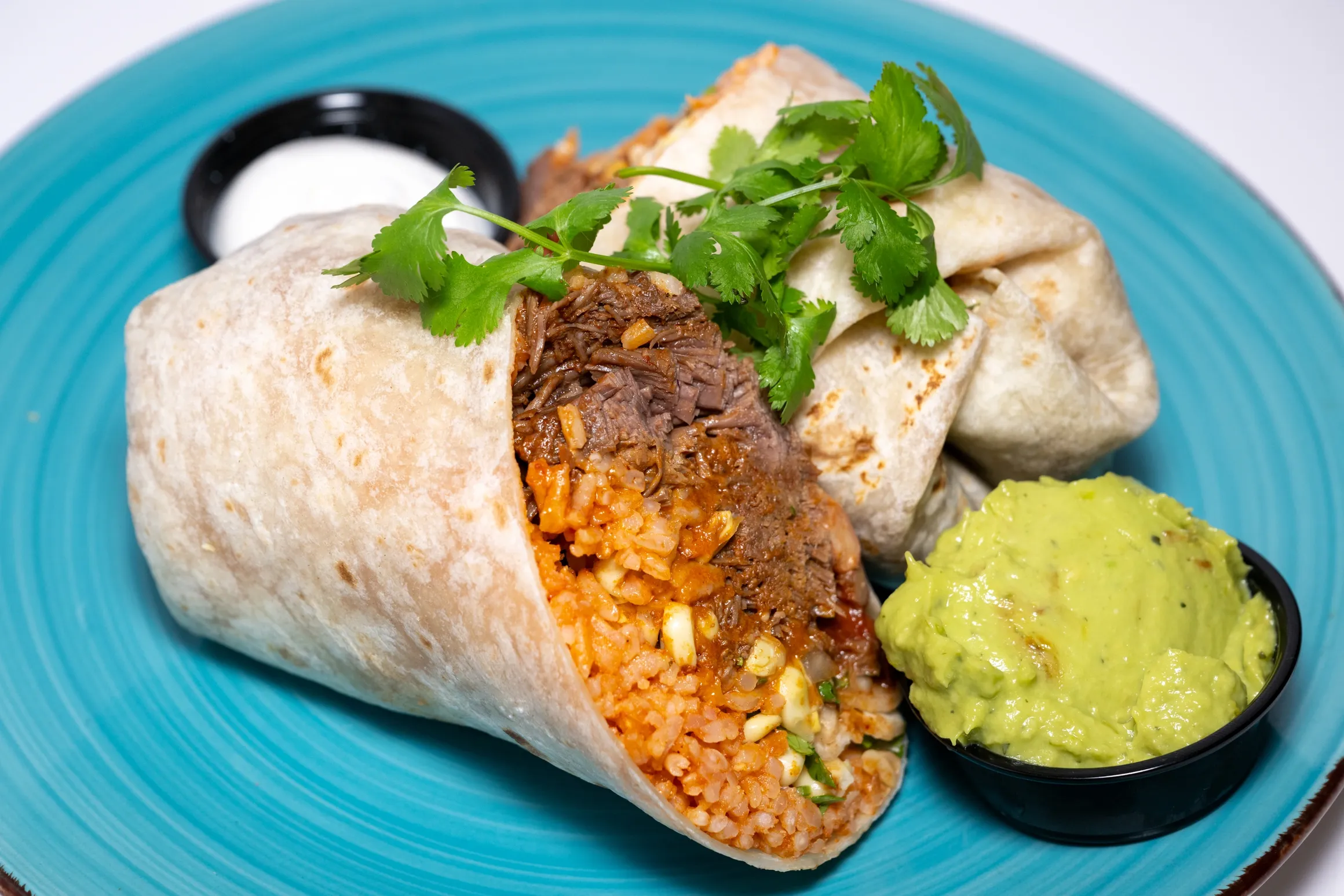 burrito with carne asada, rice, and guacamole on the side