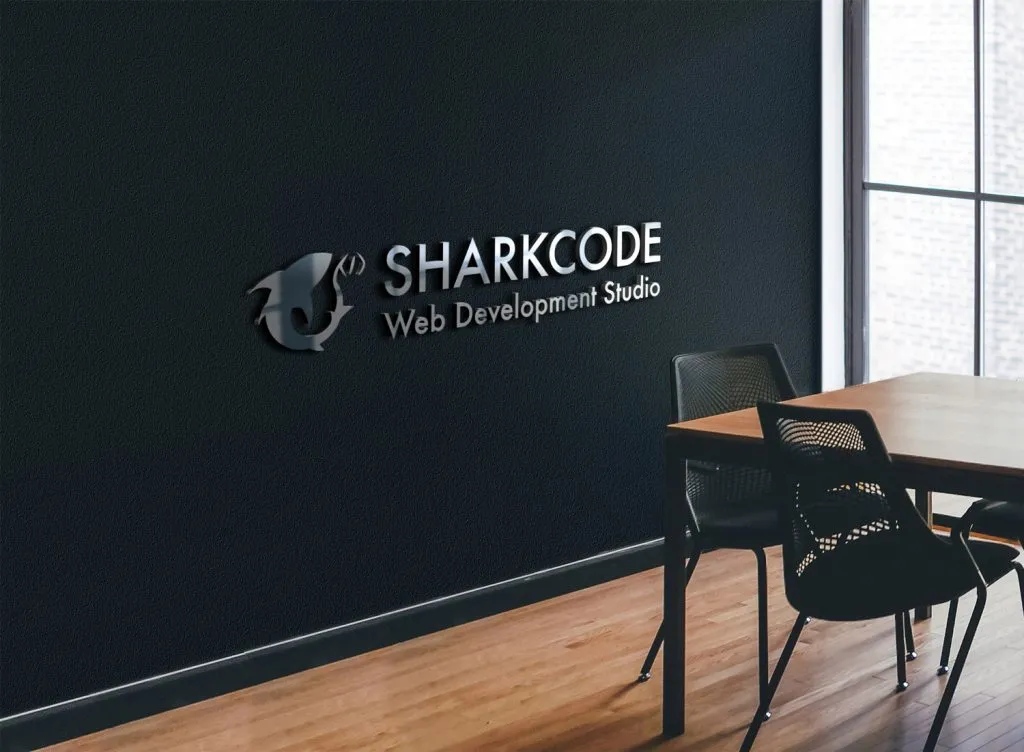 Modern office interior with a wooden table, black chairs, and a wall sign displaying a shark logo and the text 'SHARKCODE Web Development Studio'.