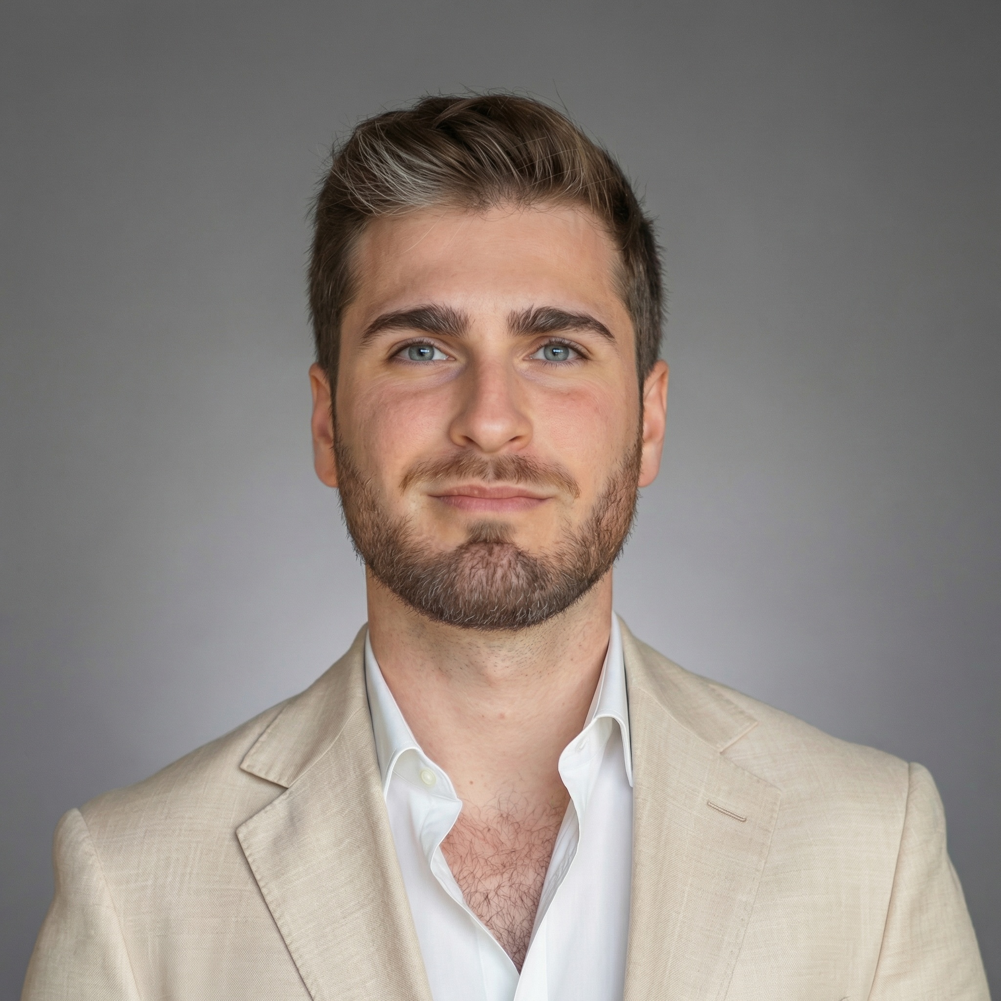 Portrait of a man with short brown hair and beard wearing a gray suit jacket and white shirt, against a light background.
