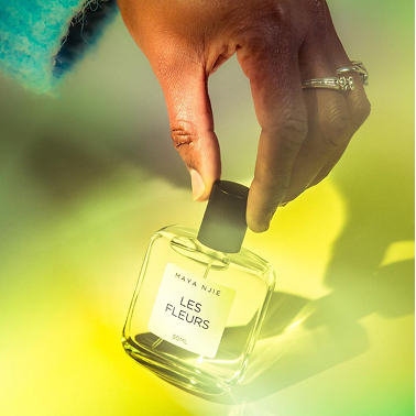 Hand holding Mayan Jie perfume bottle against green background.