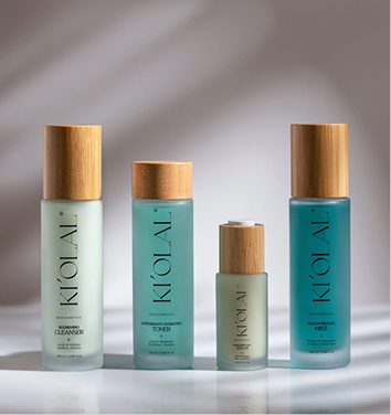 Kiolal – four frosted glass skincare bottles with wooden caps in soft green and teal tones.