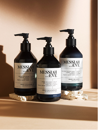 Messiah and Eve – amber body cleanser and body cream bottles with pump dispensers in warm studio light.