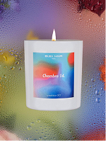 Bleu Nour – lit white candle with colourful gradient label against a softly blurred, dewy background.