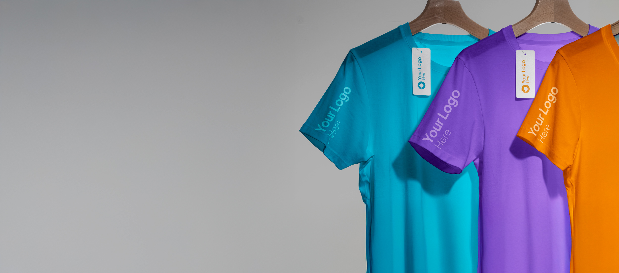 Three colorful t-shirts with tags hang on wooden hangers against a plain background.