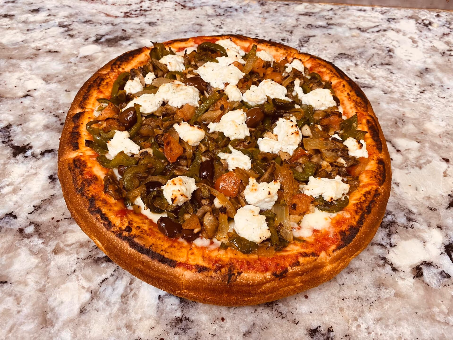 A pizza with vegetables and cheese on a marble counter.