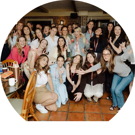 A large group of diverse young women posing and smiling energetically indoors with some making peace signs and playful gestures.