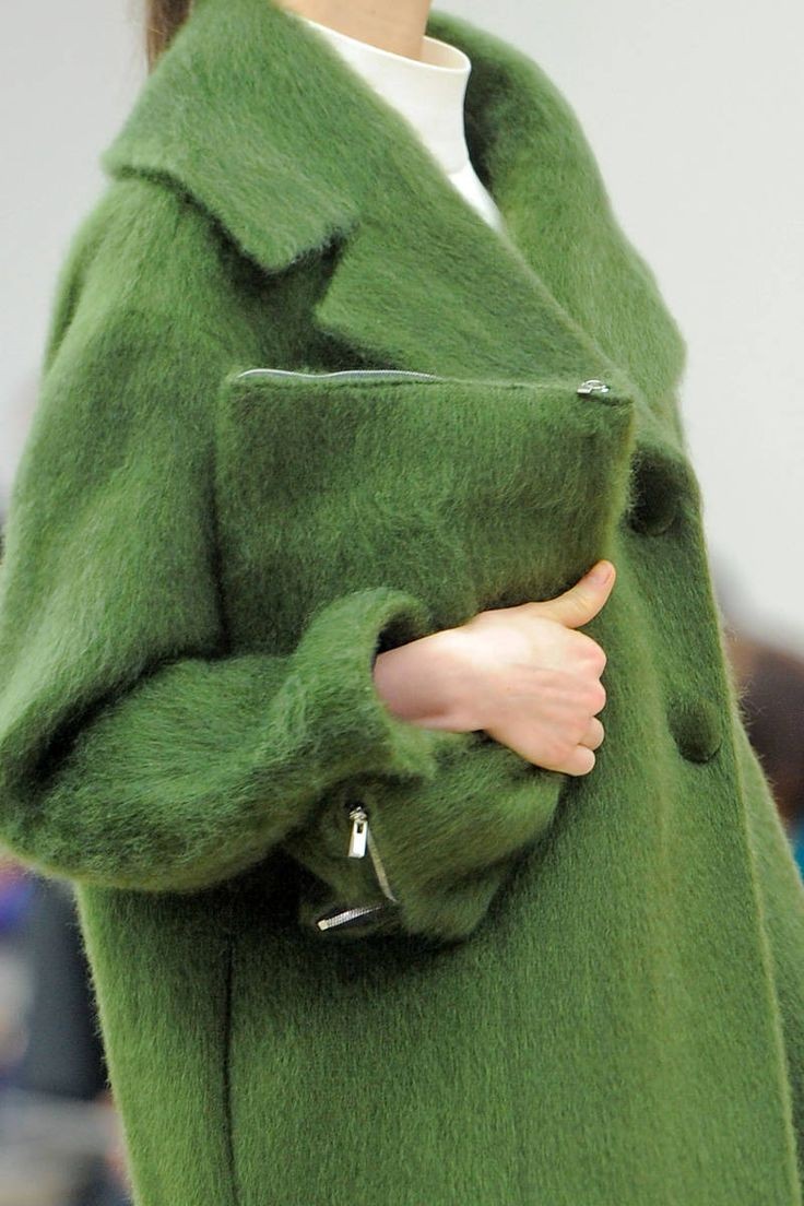 Close-up of a person wearing a fuzzy green coat and holding a matching green clutch bag.