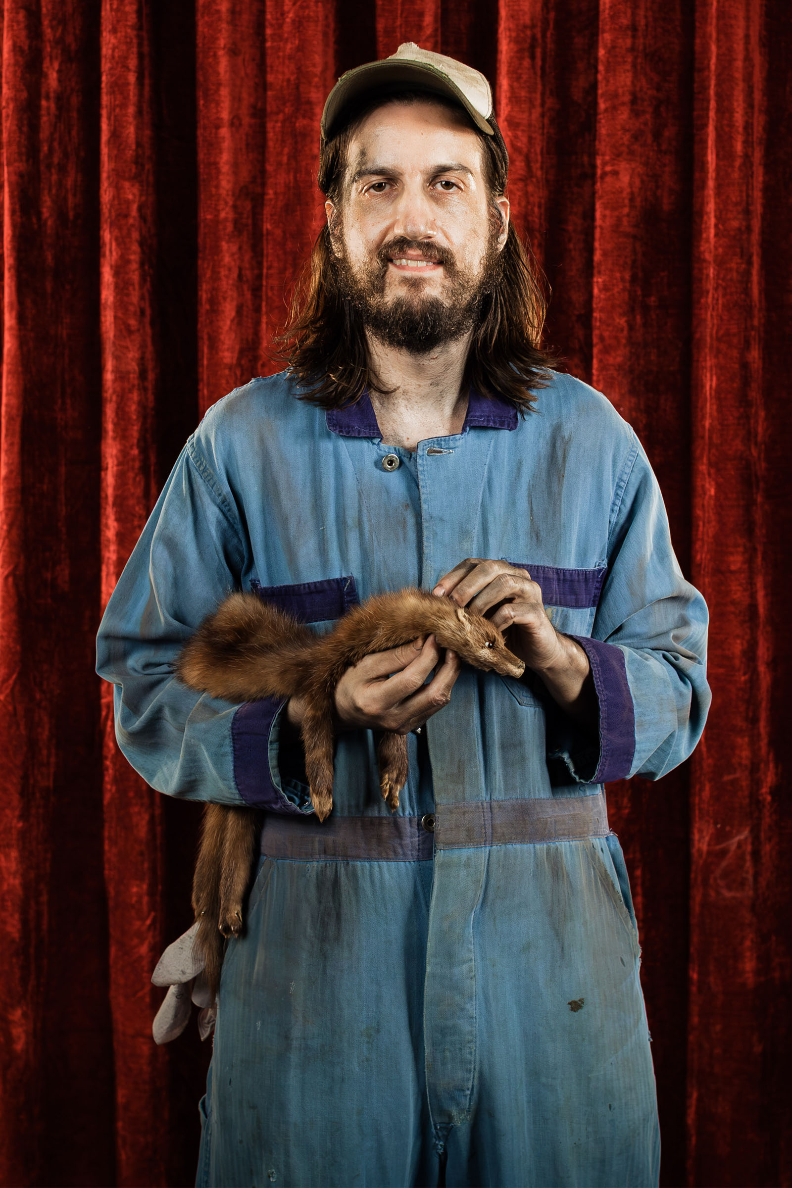 Tow truck driver portrait holding a mink while wearing work coveralls and cap, Speedy Auto campaign.