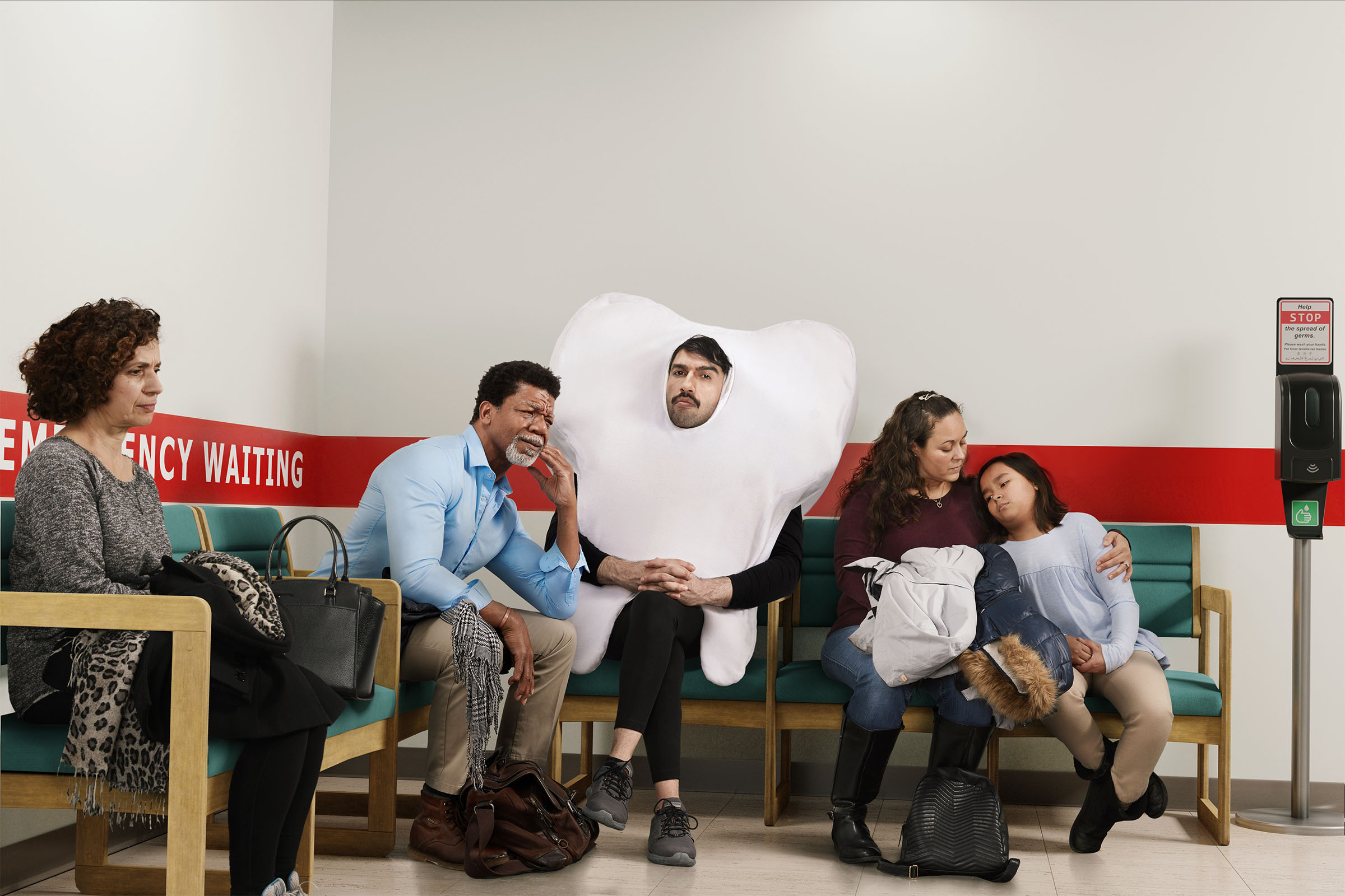 Person in tooth costume seated in hospital emergency waiting room beside patients, Ontario Dental Association campaign