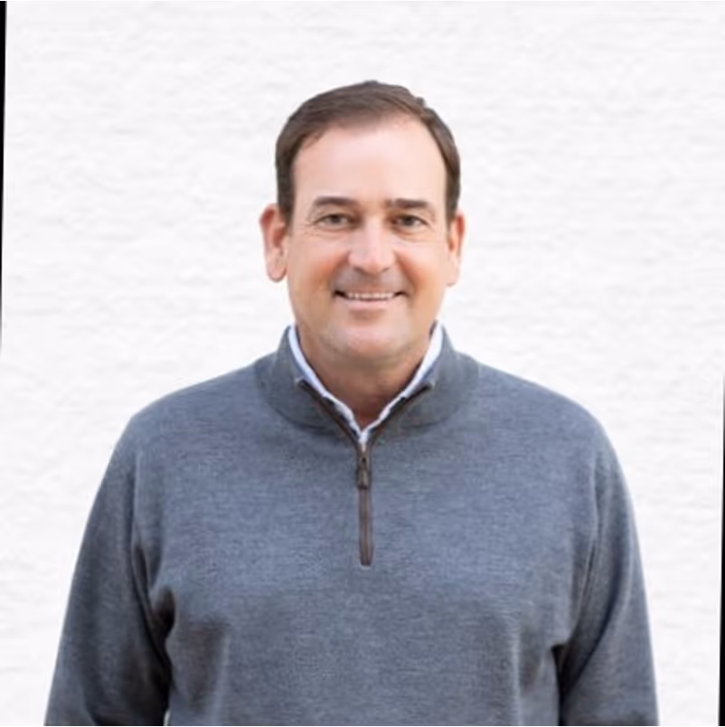 Smiling middle-aged man wearing a gray zip-up sweater standing against a white background.