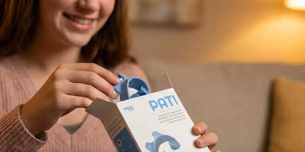 Smiling person holding a blue wristband device partially removed from a white box labeled PATI.