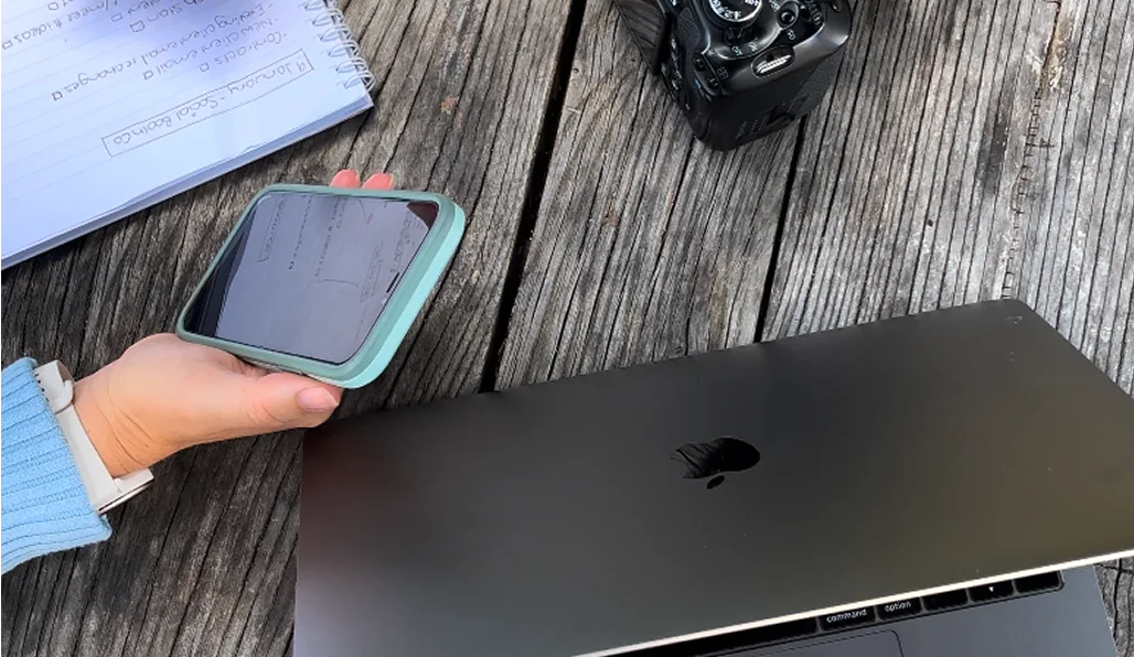 A person is holding a phone in a hand above apple macbook