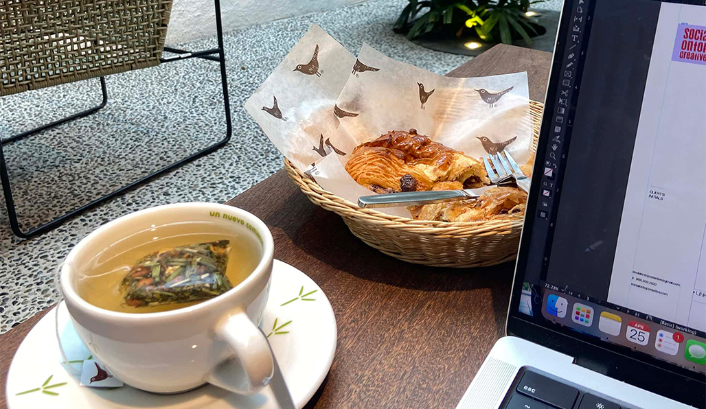 A girl wearing a yellow shirt and a beige hat is holding a glass of wine. Behind the girl you can see a pond