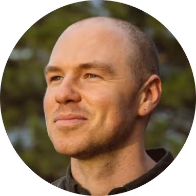 Portrait of a bald man with a slight smile looking to the side against a blurred outdoor background.