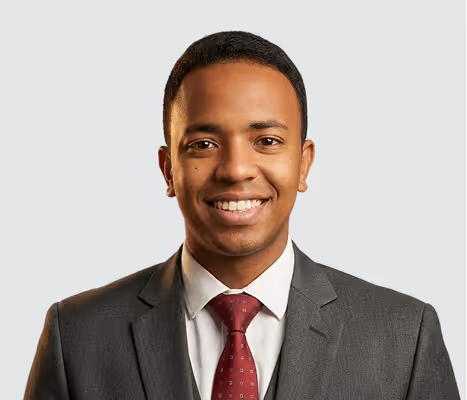 Homme souriant vêtu d'un costume gris et d'une cravate bordeaux sur fond clair.