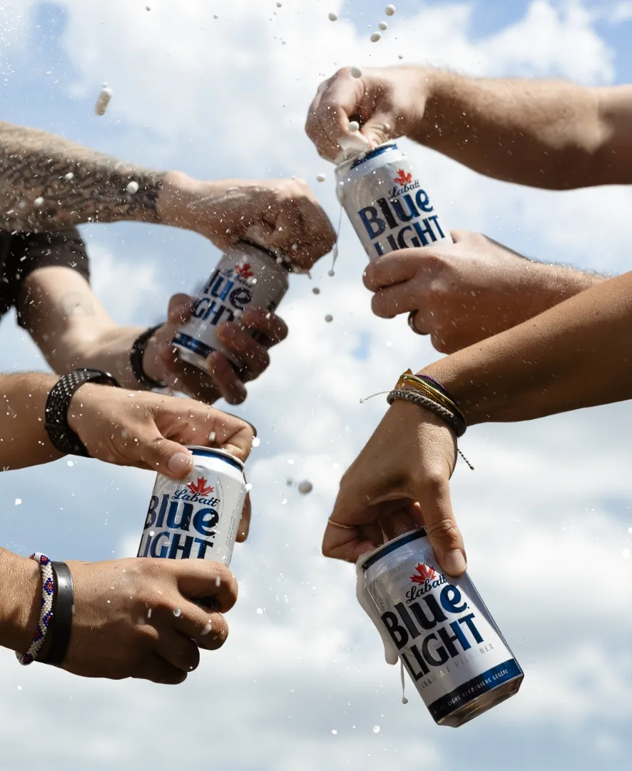 4 hands cracking Labatt Blue Light cans with a blue sky background