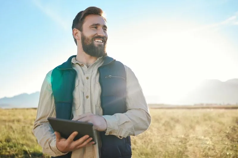 Man stood in a grass field holding a tablet