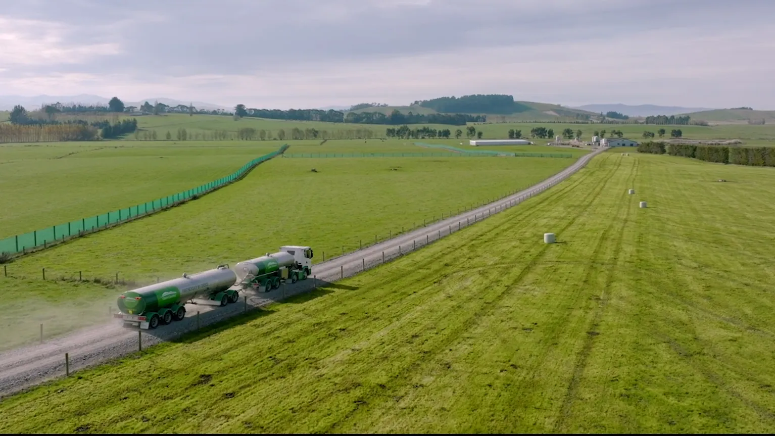 M2X and Open Country logos over a photo of an Open Country dairy tanker driving along a driveway to a dairy processing plant