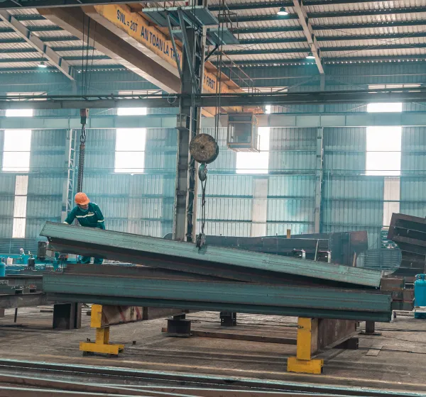 Worker in facility lifting metal beams with crane