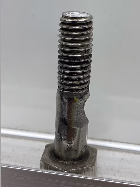 An einem Metallblock befestigte beschädigte Schraube mit abgenutztem Gewinde und Verformung am Schaft.