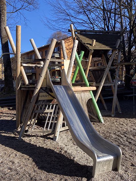Zwei Kinder spielen an einer Holzschaukelbahn in einer Berglandschaft mit bewölktem Himmel.