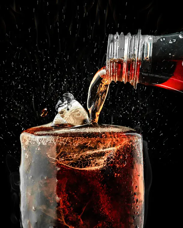Pouring cola into a glass with ice.