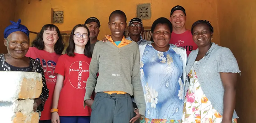 Center man in gray top stands among smiling group.