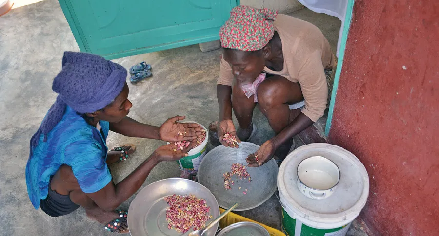 Two women sorting beans outside a doorway.