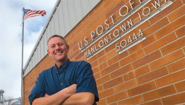 Smiling man in blue shirt in front of post office.