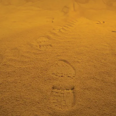 Footprints in sand along a path under orange light