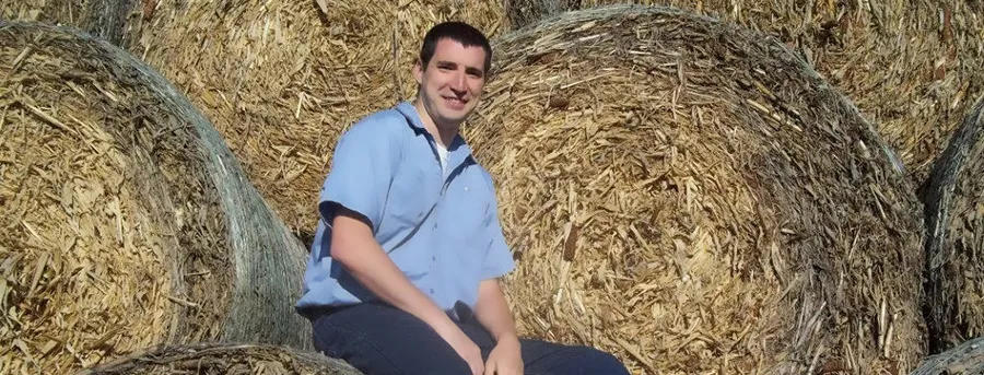 Mike Richardson sits on a round hay bale among stacked bales